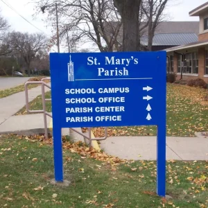 A post and panel sign for a church that shows the directions to buildings.