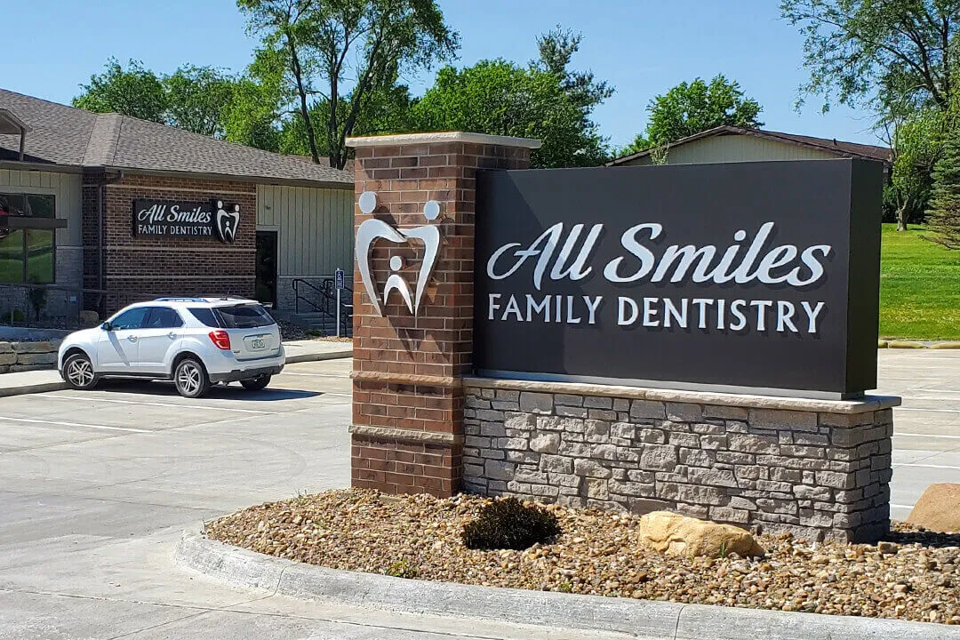 A monument sign for a dentist office with the building in the background.