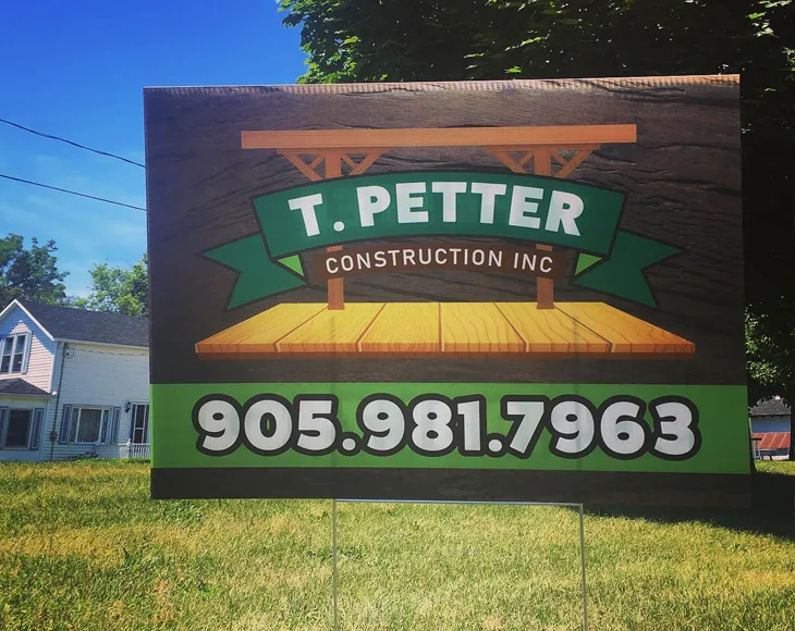 A corrugated plastic lawn sign that advertises a construction company, installed on grass.