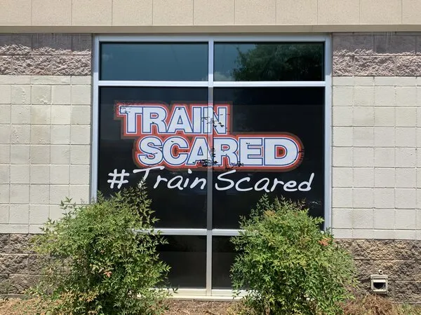 A window of a gym, with window graphics that says train scared.