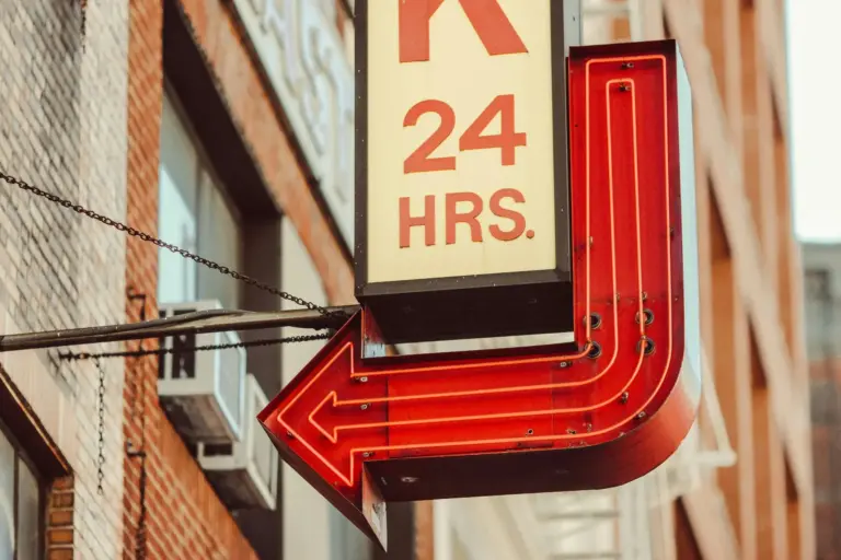 A sign on a building that advertises 24 hours with neon tube arrow pointing towards the building.